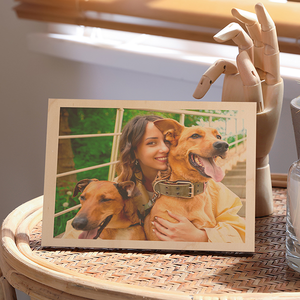 Wooden photo frame with a picture of a woman and two dogs on a table. Custom wood photo print with natural grain texture